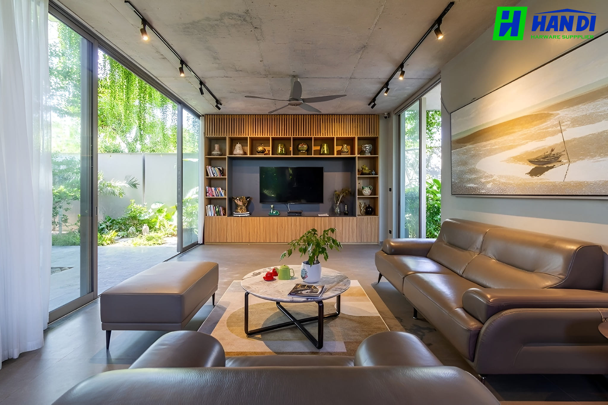 Thiết kế phòng khách biệt thự Green Villa phong cách Eco-Modern với trần bê tông mài thô, sofa da màu nâu ấm áp và hệ cửa kính lùa bản lớn mở toang hướng ra sân vườn xanh mát.